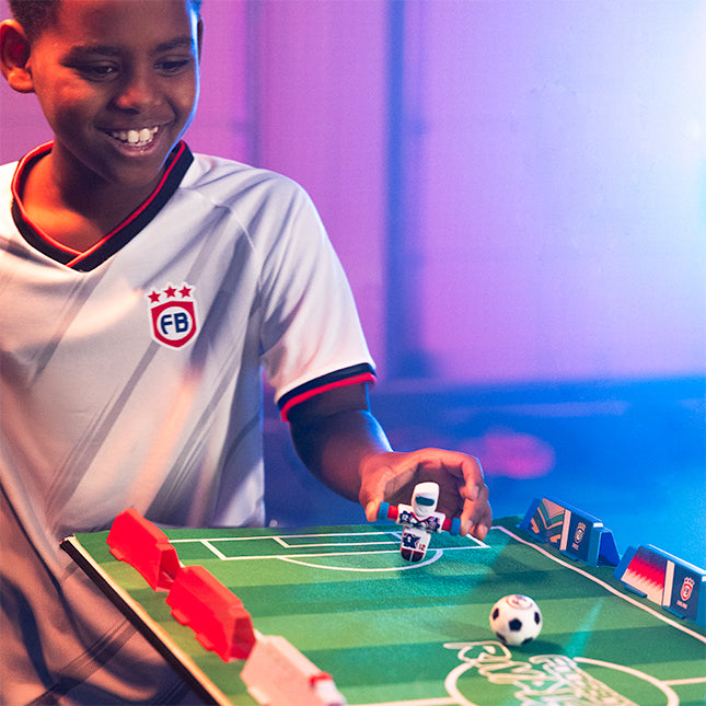 Child playing with a toy soccer game on a table with a colorful background