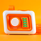 A white and orange electronic sensory toy device with a round white dial, four green illuminated buttons, and a small row of blue indicator lights, shown on a solid orange background.
