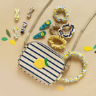 Striped pouch with lemon design surrounded by hair accessories on a beige background
