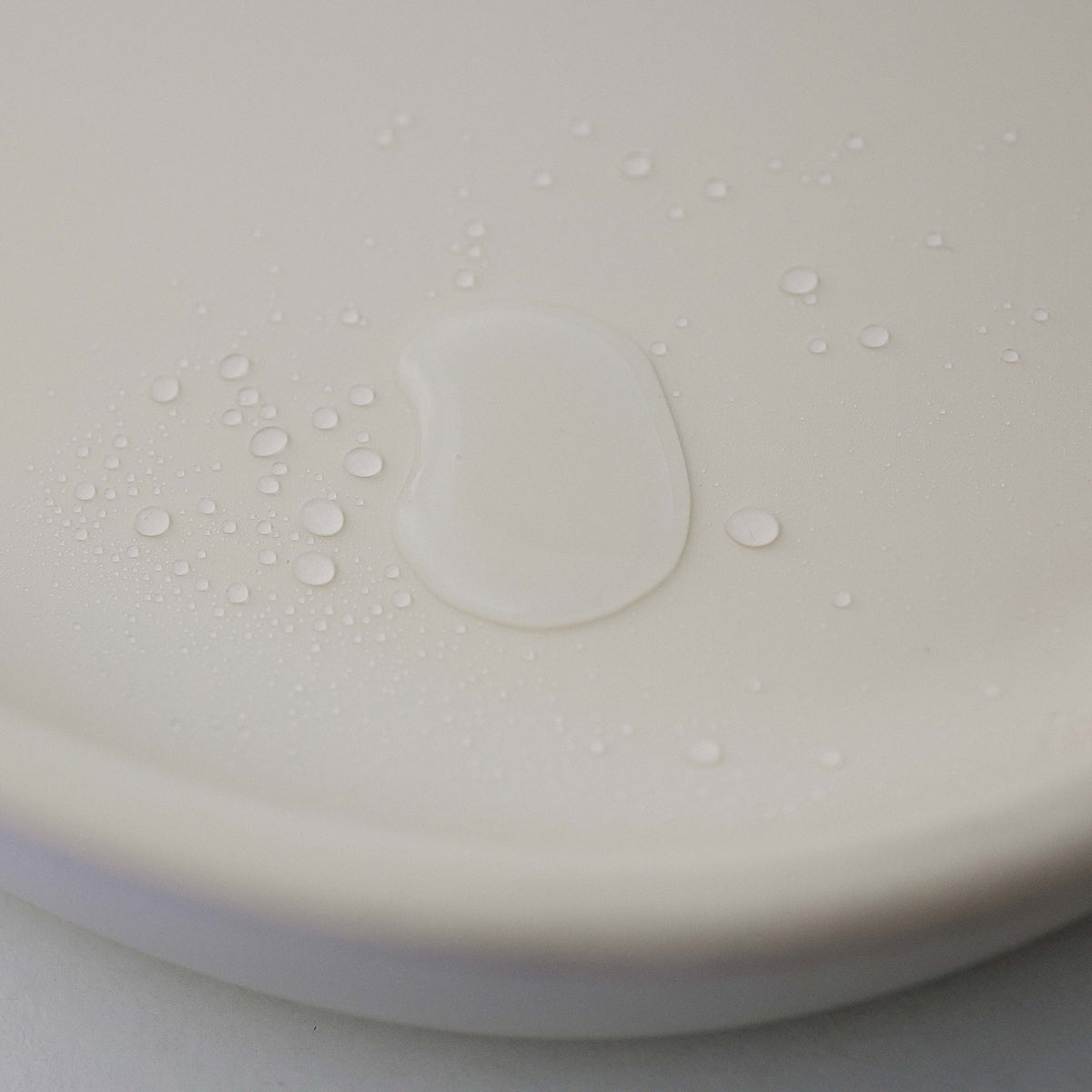 Close-up of a white plastic component with water droplets on a light gray background