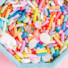 Assorted colorful sprinkles in a container on a pink background