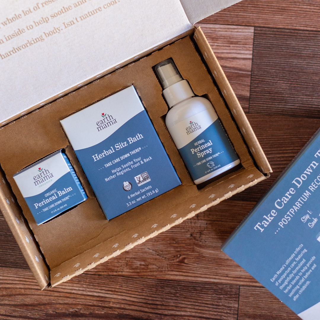 Earth Mama postpartum care kit with balm, spray, and book on a wooden surface