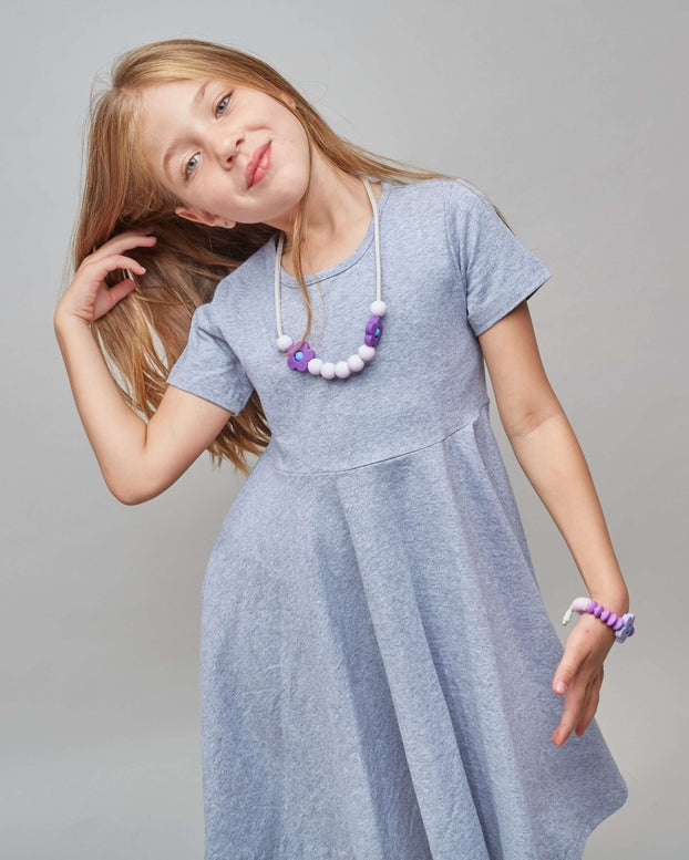 Young girl wearing a light blue dress with a necklace on a gray background