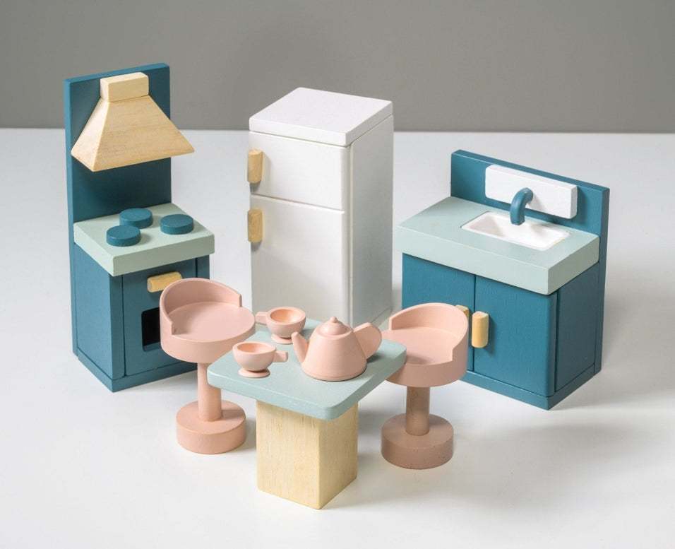 Wooden kitchen furniture set by Mentari against a white background, featuring a blue stove with an oven and hood, a white refrigerator with wooden handles, a blue sink unit with a cupboard, and a light wood-colored square table surrounded by four matching pinkish-tan stools.