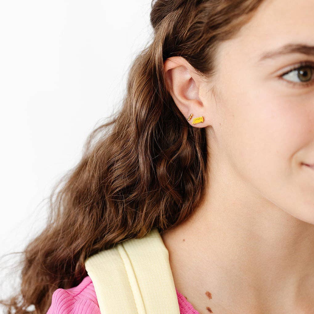Close-up of a woman wearing yellow stud earrings with a plain background
