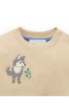 A close-up of a beige knit baby sweater featuring an embroidered gray and white wolf holding green leaves on the chest.