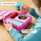 Child interacting with a pink lunch box containing food on a wooden surface