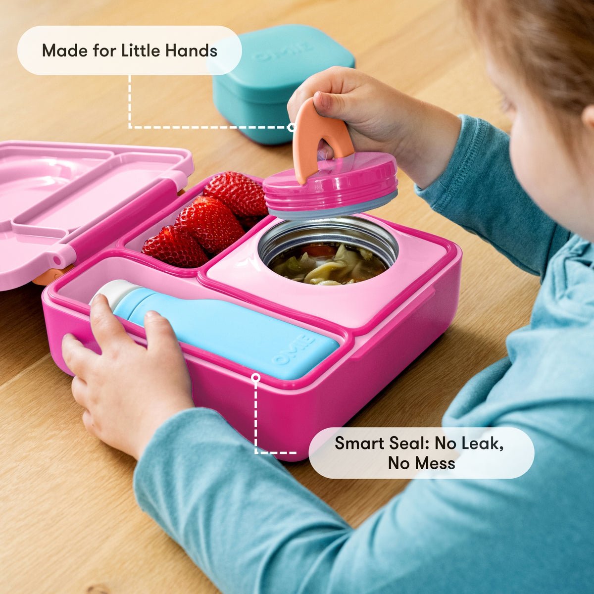 Child interacting with a pink lunch box containing food on a wooden surface
