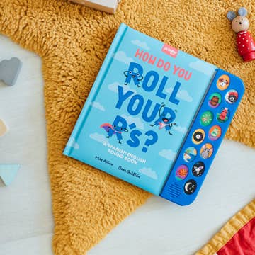Children's book titled 'How Do You Roll Your D's?' on a yellow textured surface with toys around.