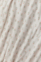 A close-up of a cream-colored fabric with a delicate, repeating pattern of small pink flowers and green leaves, draped in soft folds.