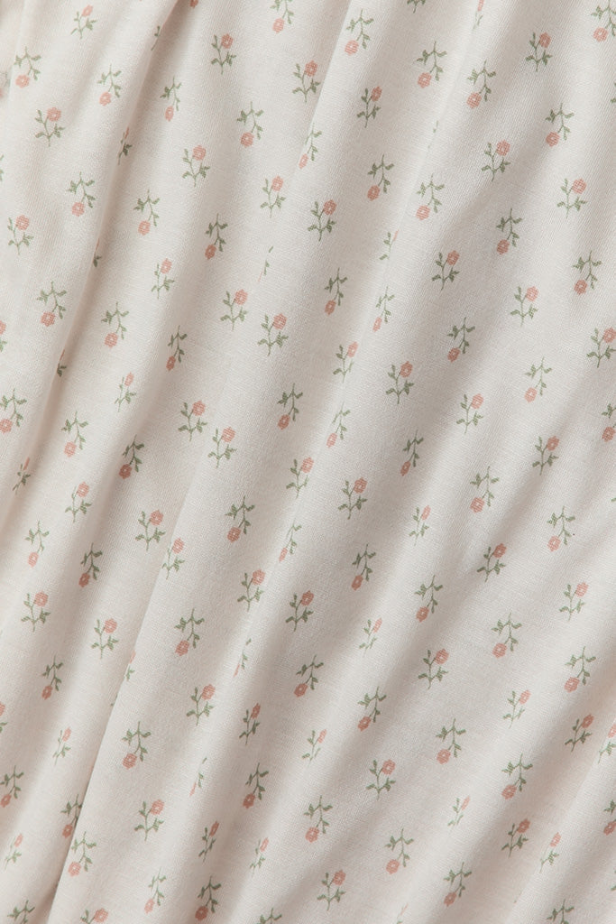 A close-up of a cream-colored fabric with a delicate, repeating pattern of small pink flowers and green leaves, draped in soft folds.