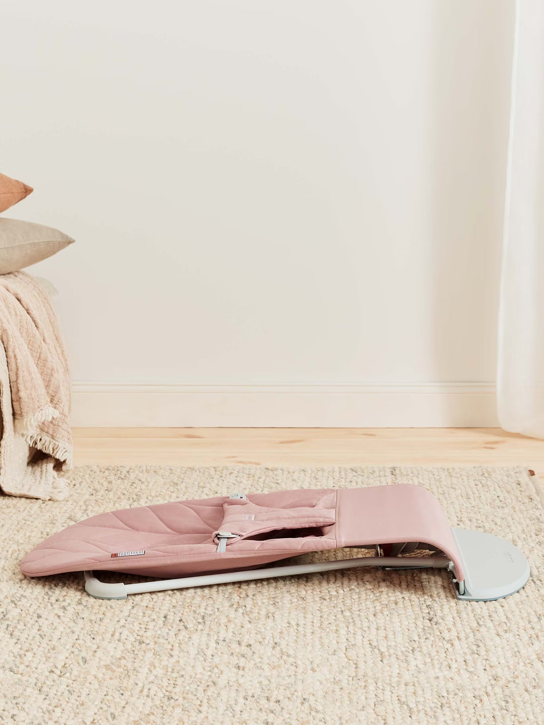 Pink baby bouncer on a beige carpet with a neutral-colored wall in the background