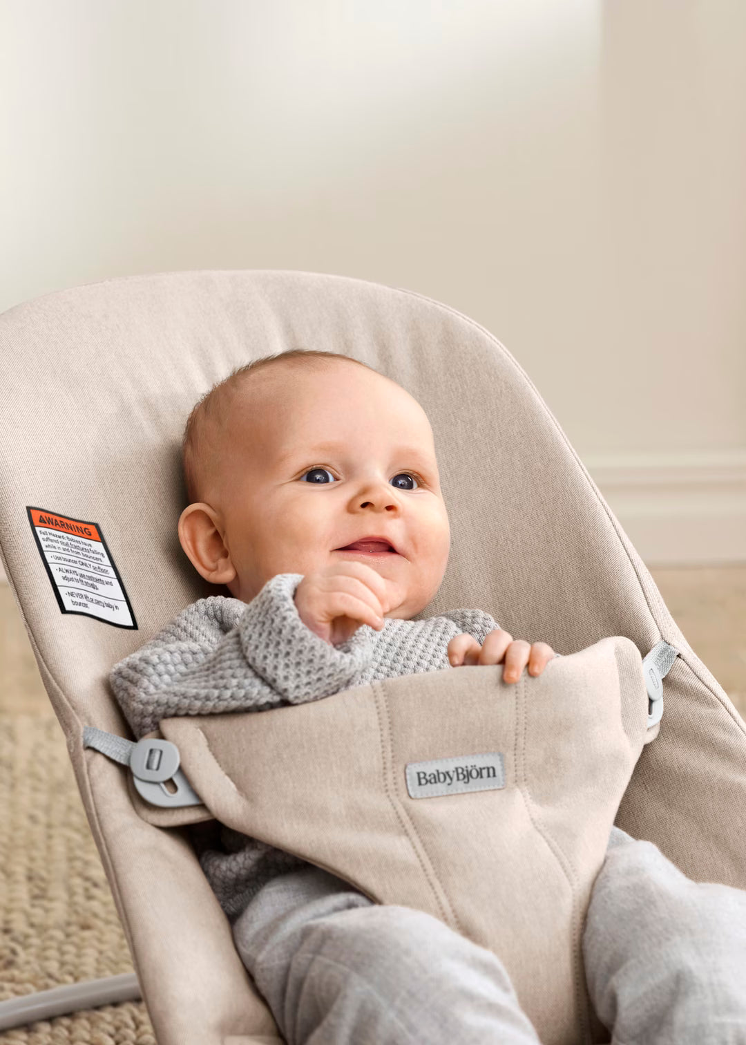 Baby in a beige BabyBjörn baby bouncer with a neutral background
