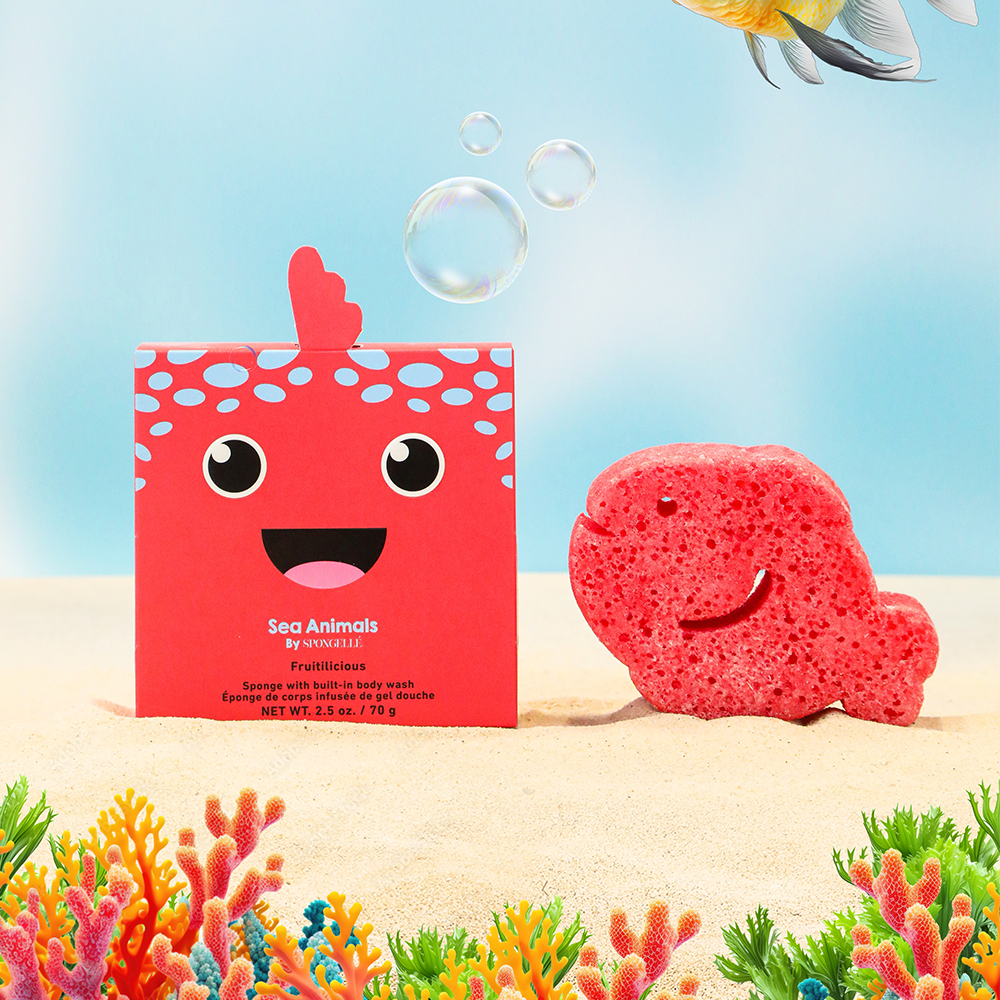 Red whale-shaped bath sponge with a matching box on a sandy beach with coral and water background