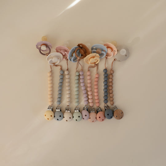 Set of colorful baby pacifiers with beaded straps on a beige background
