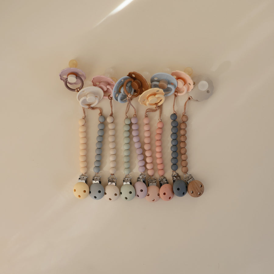 Set of colorful baby pacifiers with beaded straps on a beige background