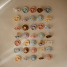 Collection of colorful pacifiers arranged in a grid on a beige surface