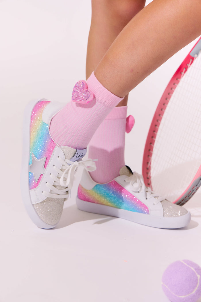 White sneakers with rainbow patterns and pink socks worn by a person on a light background