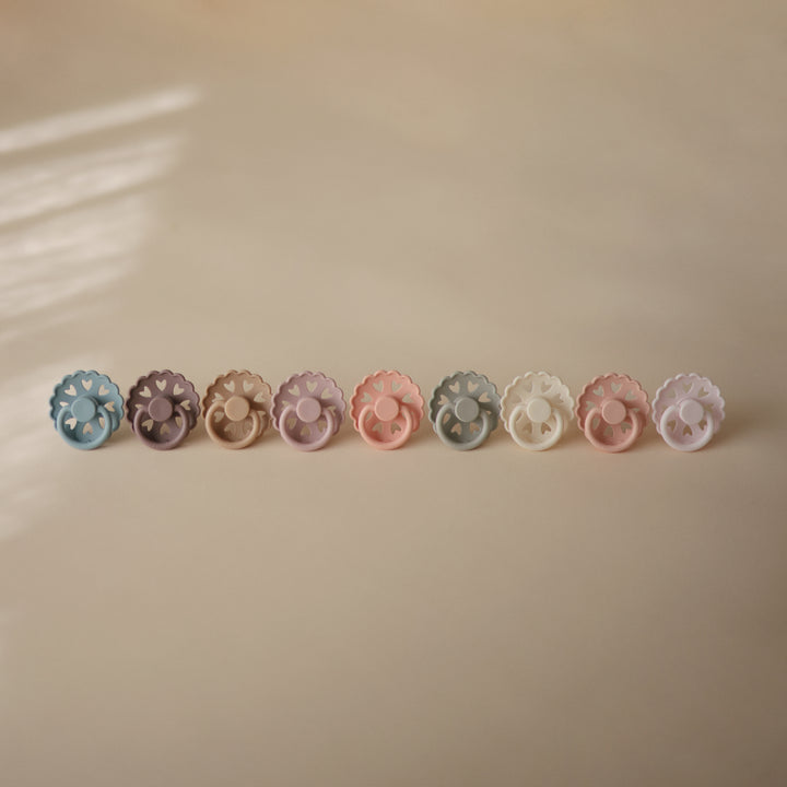 Row of colorful pacifiers on a beige background