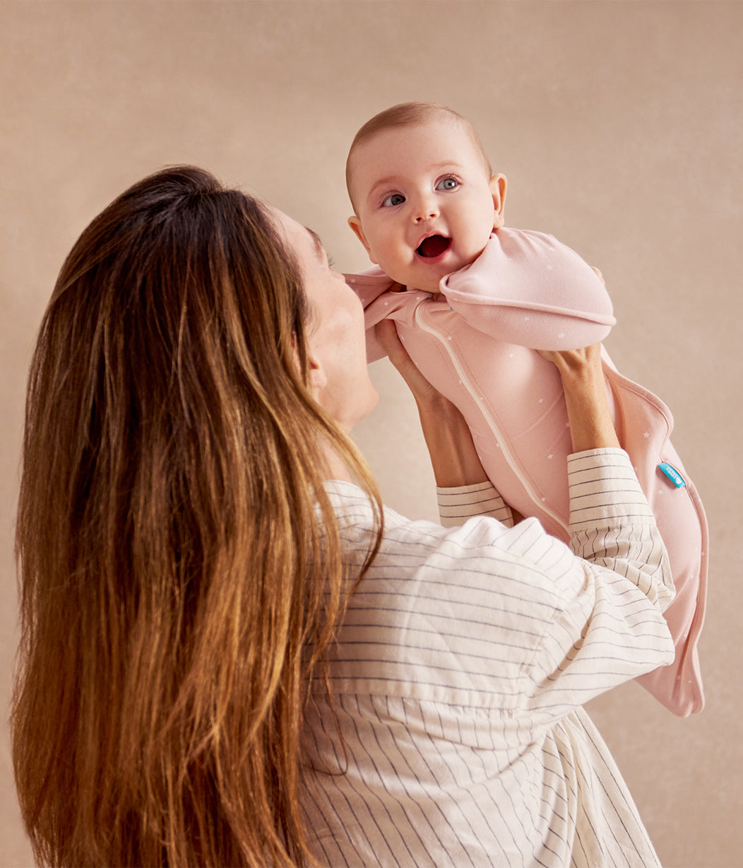 Woman holding a baby wrapped in a pink blanket against a beige background