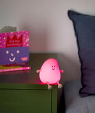 Pink character light on a nightstand with a purple pillow and birthday card in the background