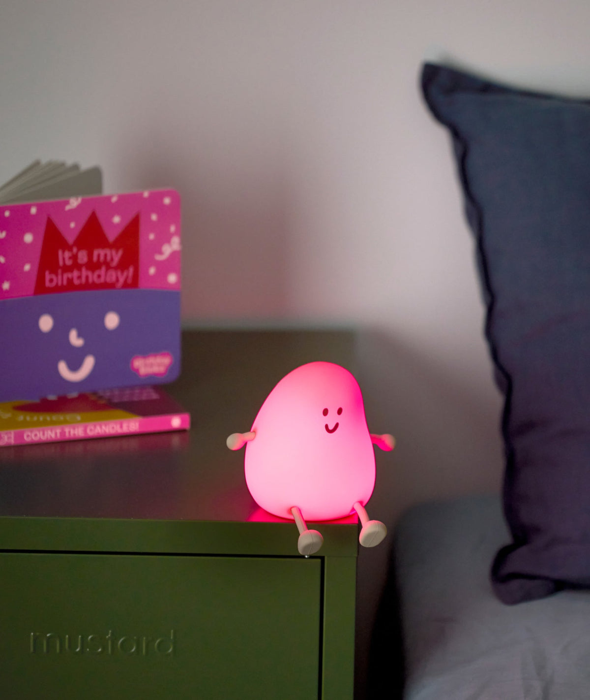 Pink character light on a nightstand with a purple pillow and birthday card in the background