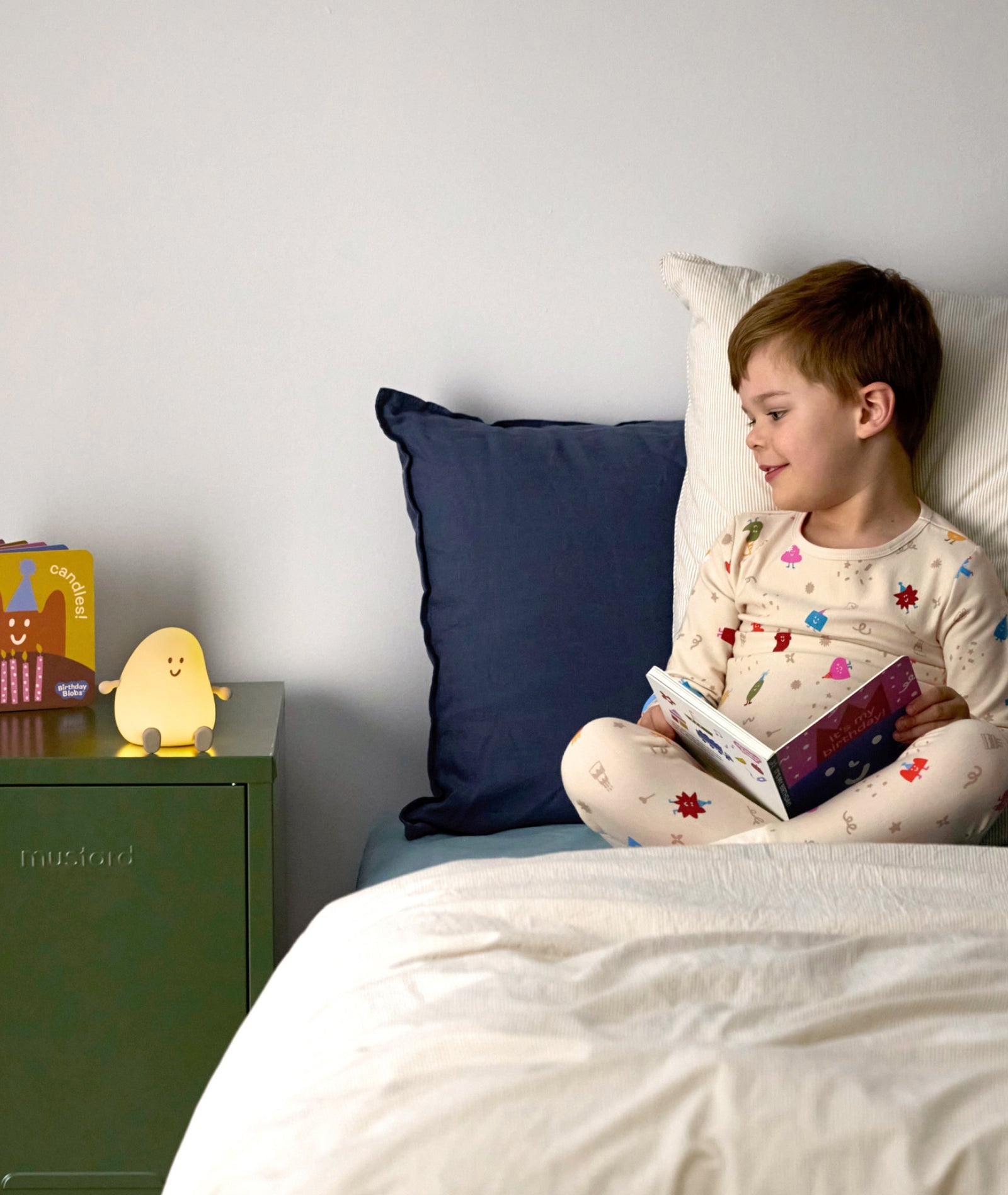 Child reading a book in bed with a nightlight and colorful pillow