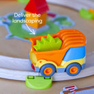 Colorful toy truck with green cargo on a wooden surface, labeled 'Deliver the landscaping'.