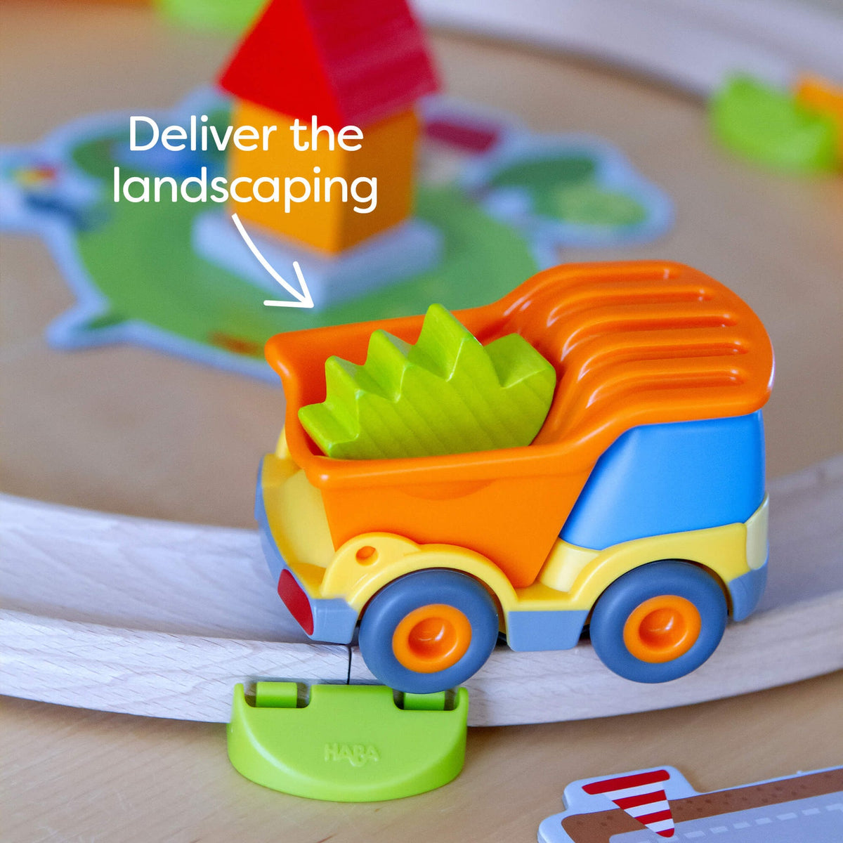 Colorful toy truck with green cargo on a wooden surface, labeled 'Deliver the landscaping'.