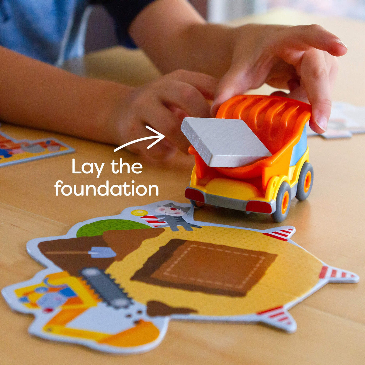 Child playing with a toy dump truck on a wooden surface with educational cards.