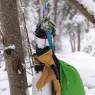 Hanging items including a water bottle, gloves, and a green bag in a snowy forest setting.