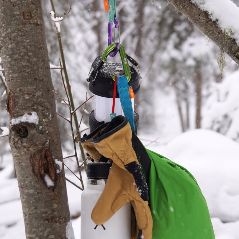 Hanging items including a water bottle, gloves, and a green bag in a snowy forest setting.