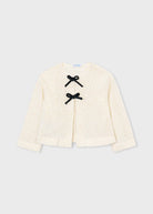 An off-white textured teddy fleece cardigan with three black bow details on the front, displayed flat against a light gray background.