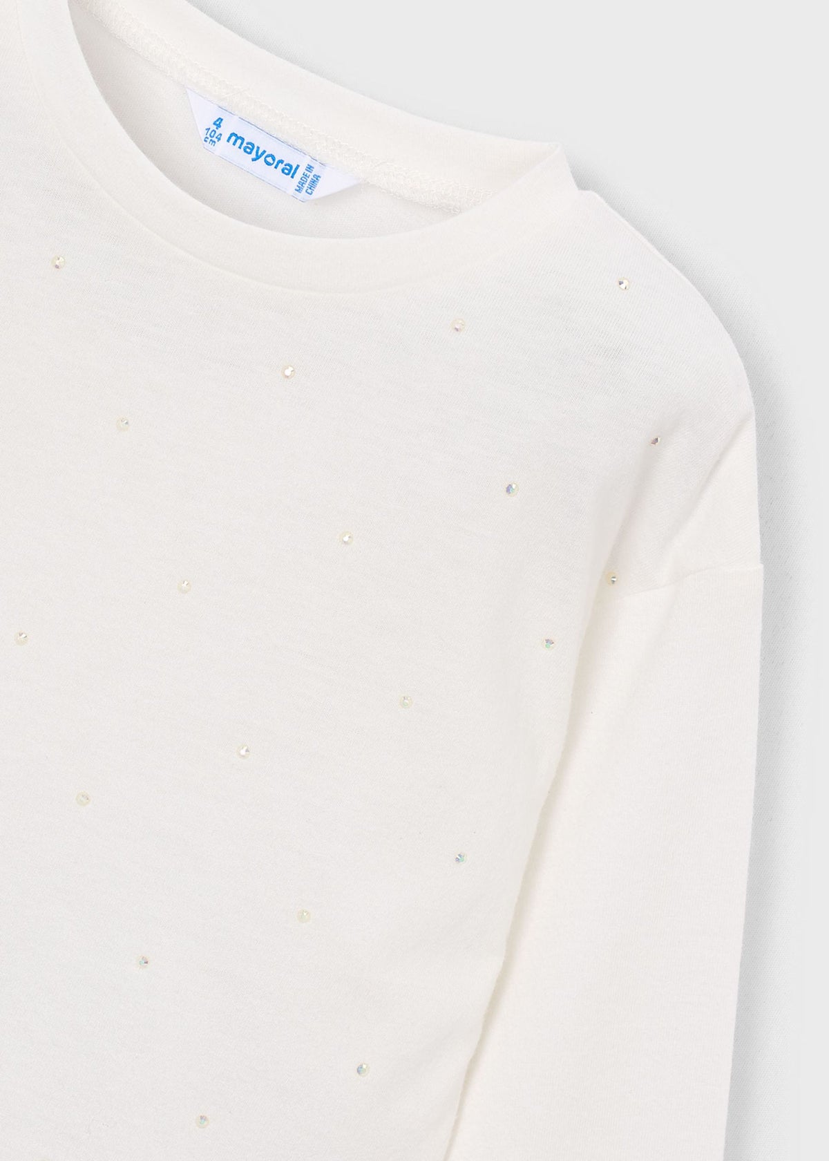 Close-up of a cream-colored long-sleeve top by Mayoral, featuring a subtle dotted pattern of small metallic studs and a visible brand label at the collar.