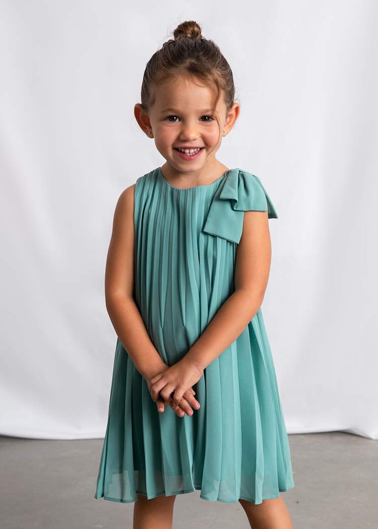 Young girl wearing a teal dress with a bow on a white background
