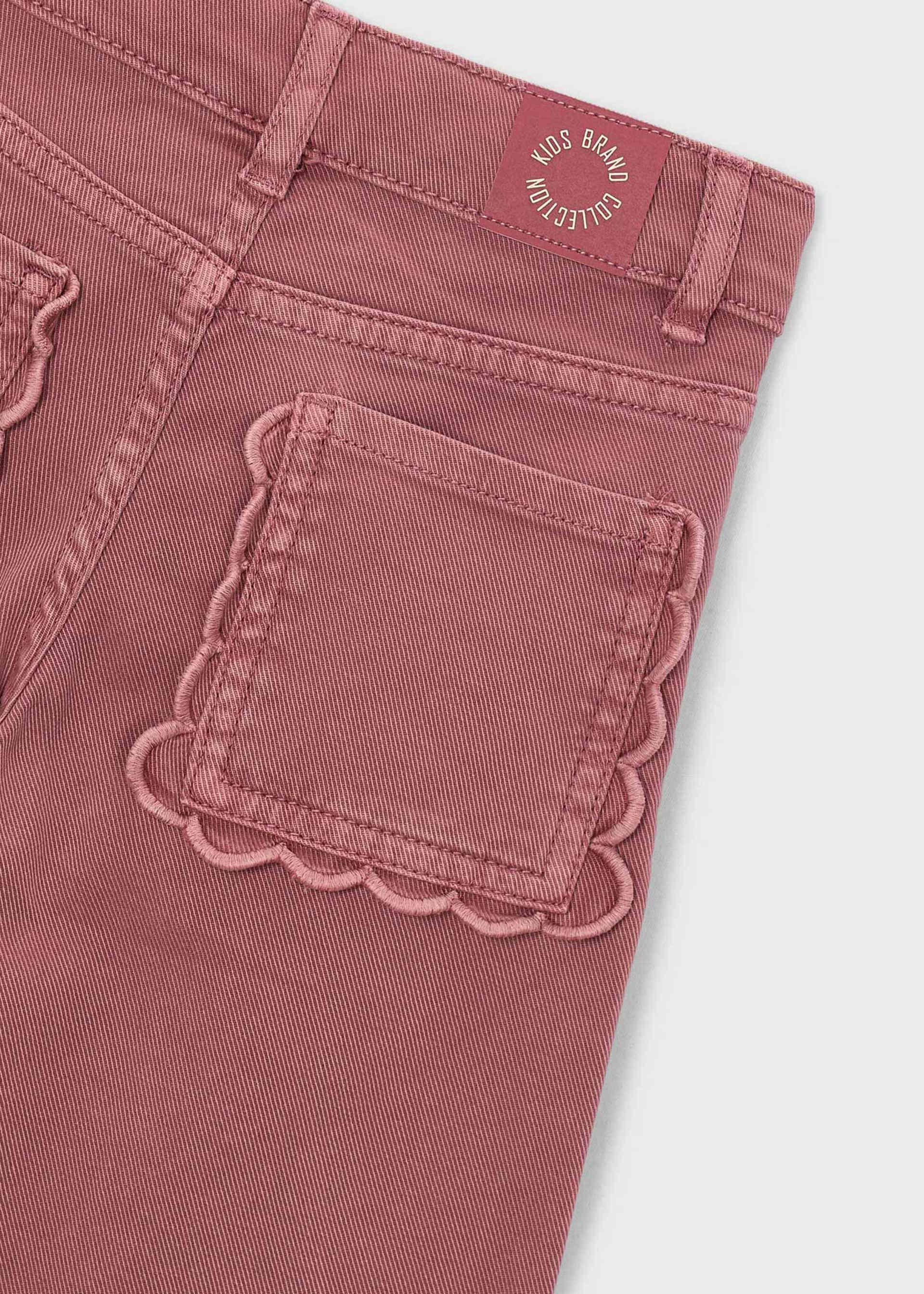 Close-up of pink pants with scalloped edge pocket on a light gray background