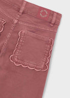 Close-up of pink pants with scalloped edge pocket on a light gray background
