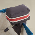 Gray cushion with red and white stripes held by blue gloves on a beige background