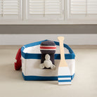 A children's nautical-themed play boat set on a white background, featuring a fabric boat with blue and cream stripes, a red life preserver, a wooden paddle, and a small black motor attachment.