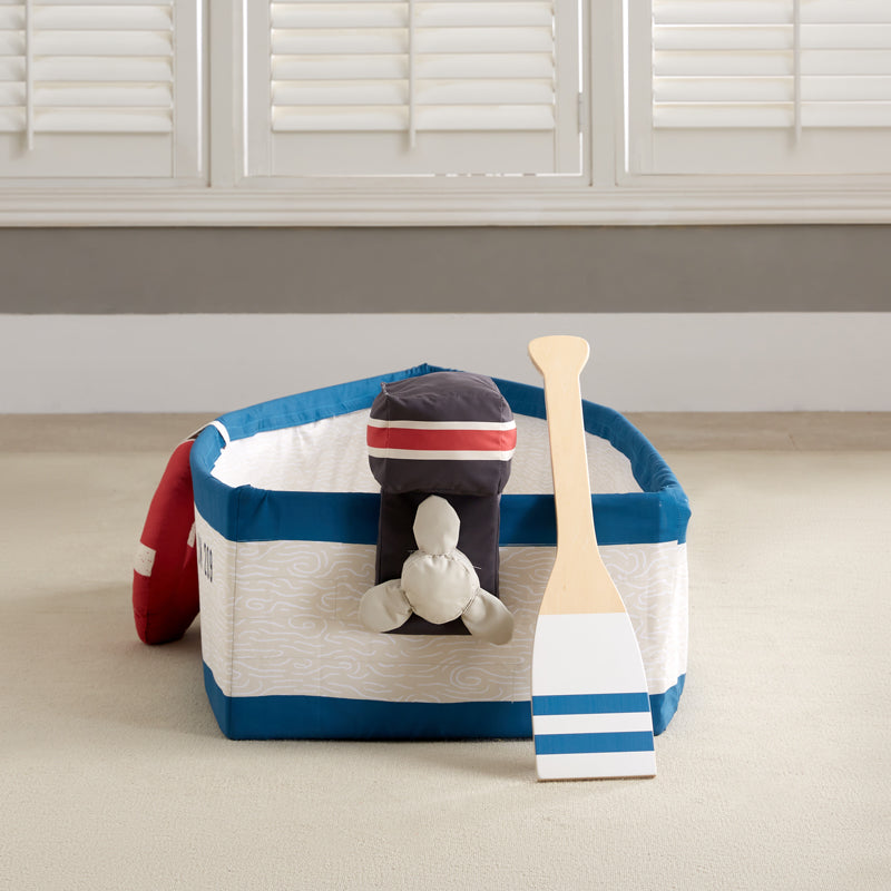 A children's nautical-themed play boat set on a white background, featuring a fabric boat with blue and cream stripes, a red life preserver, a wooden paddle, and a small black motor attachment.