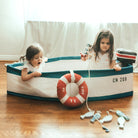 Two children playing with a toy boat on a wooden floor.