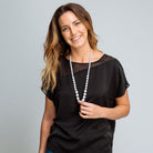 Woman wearing a black top and pearl necklace against a gray background