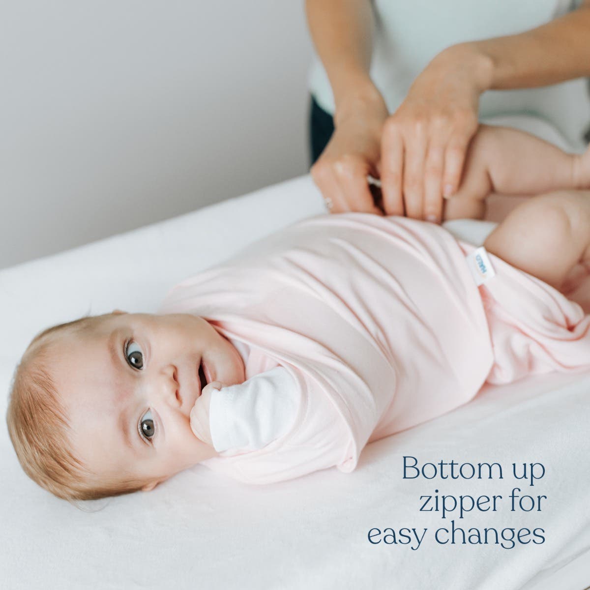 Baby lying on a changing table with a pink outfit, being changed by an adult.