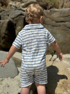 Child wearing a blue and white striped outfit standing on a rocky beach.