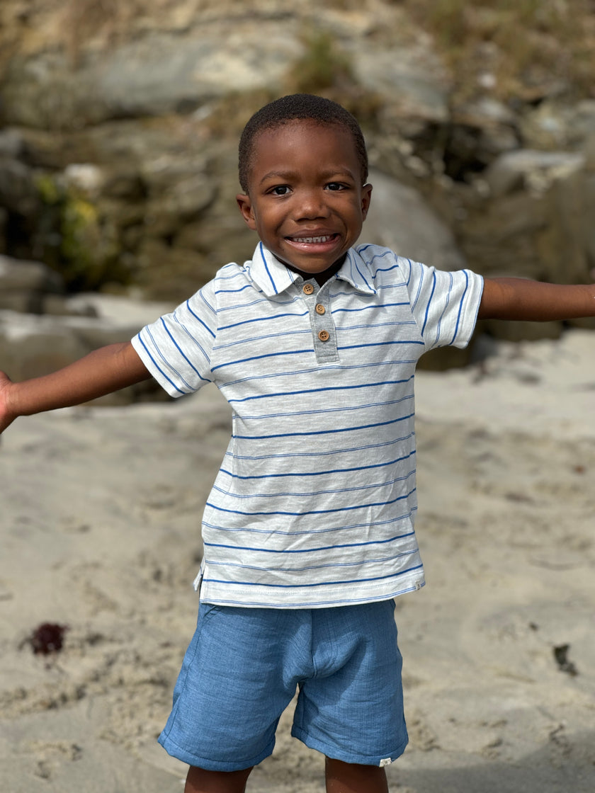 Child wearing a striped shirt and shorts standing on a rocky beach.