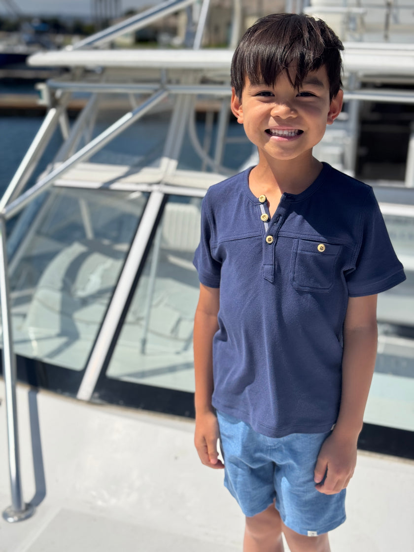 Child wearing a navy blue shirt and light blue shorts standing on a boat deck.