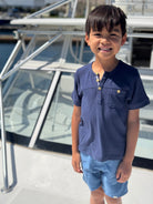 Child wearing a navy blue shirt and light blue shorts standing on a boat deck.
