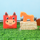 Carrot-shaped horse toy on a hay bale with a red box featuring a horse design in the background.