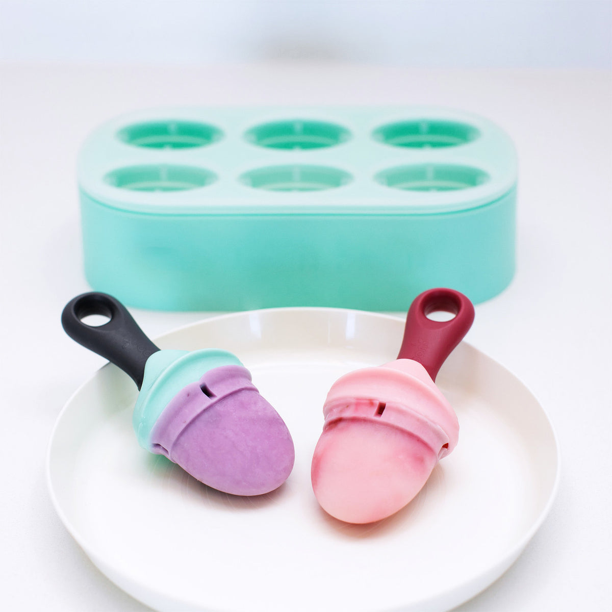 Two colorful ice cream molds on a white plate with a green ice cream mold in the background.