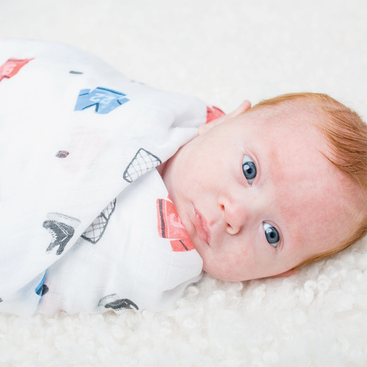 Baby lying on a white blanket wearing a patterned outfit.